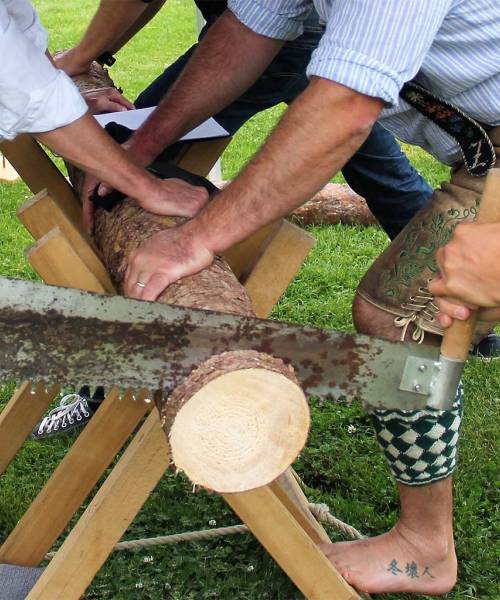 Männer halten einen Holzstamm in einer Vorrichtung, während das Stück Holz gesägt wird.