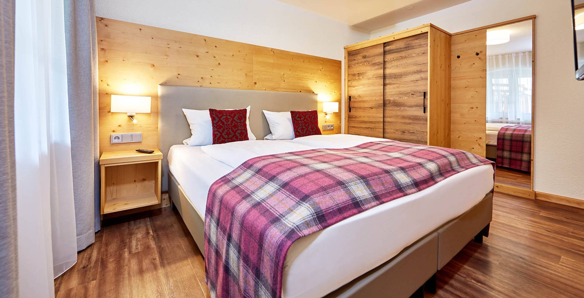 Gemütliches Doppelbett im Hotelzimmer des Berghotels Hammersbach mit modernem Komfort und Alpenblick.