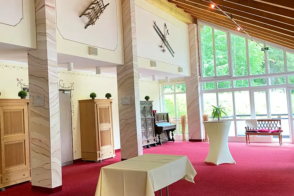 Veranstaltungsraum im Berghotel Hammersbach mit hohen Decken, Fensterfront und roten Teppichboden.