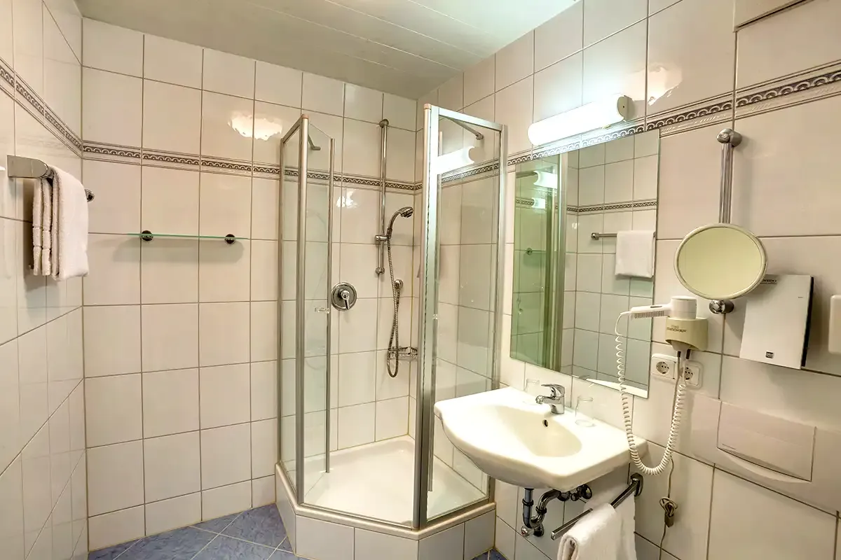 Großes helles Badezimmer im Berghotel Hammersbach mit Dusche, Spiegel und Föhn.