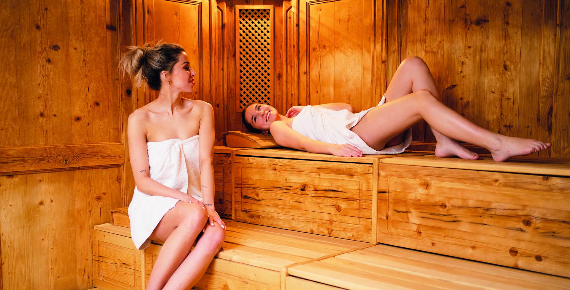 Zwei Frauen befinden sich in einer Holzsauna und unterhalten sich dabei.