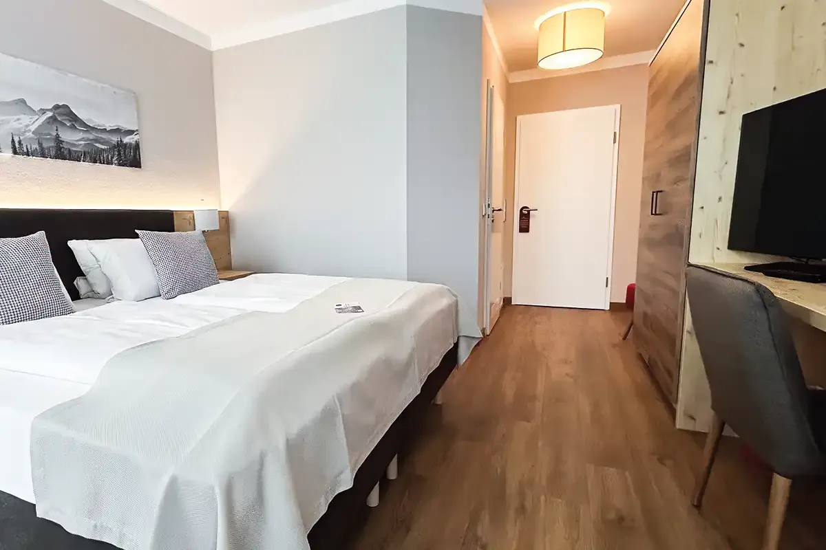Modernes Hotelzimmer im Berghotel Hammersbach mit großen Doppelbett, Scheibtisch und Kleiderschrank.