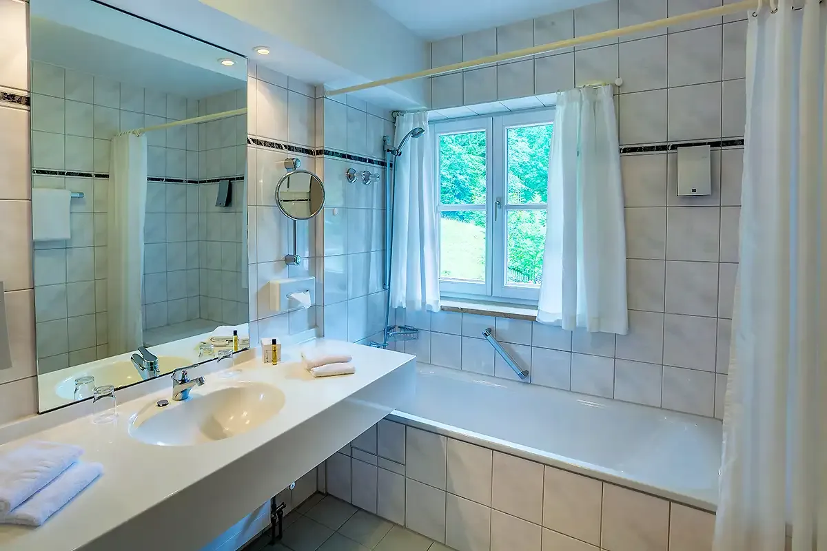 Helles Badezimmer mit Badewanne, großer Waschkommode und Spiegel im Berghotel Hammersbach.
