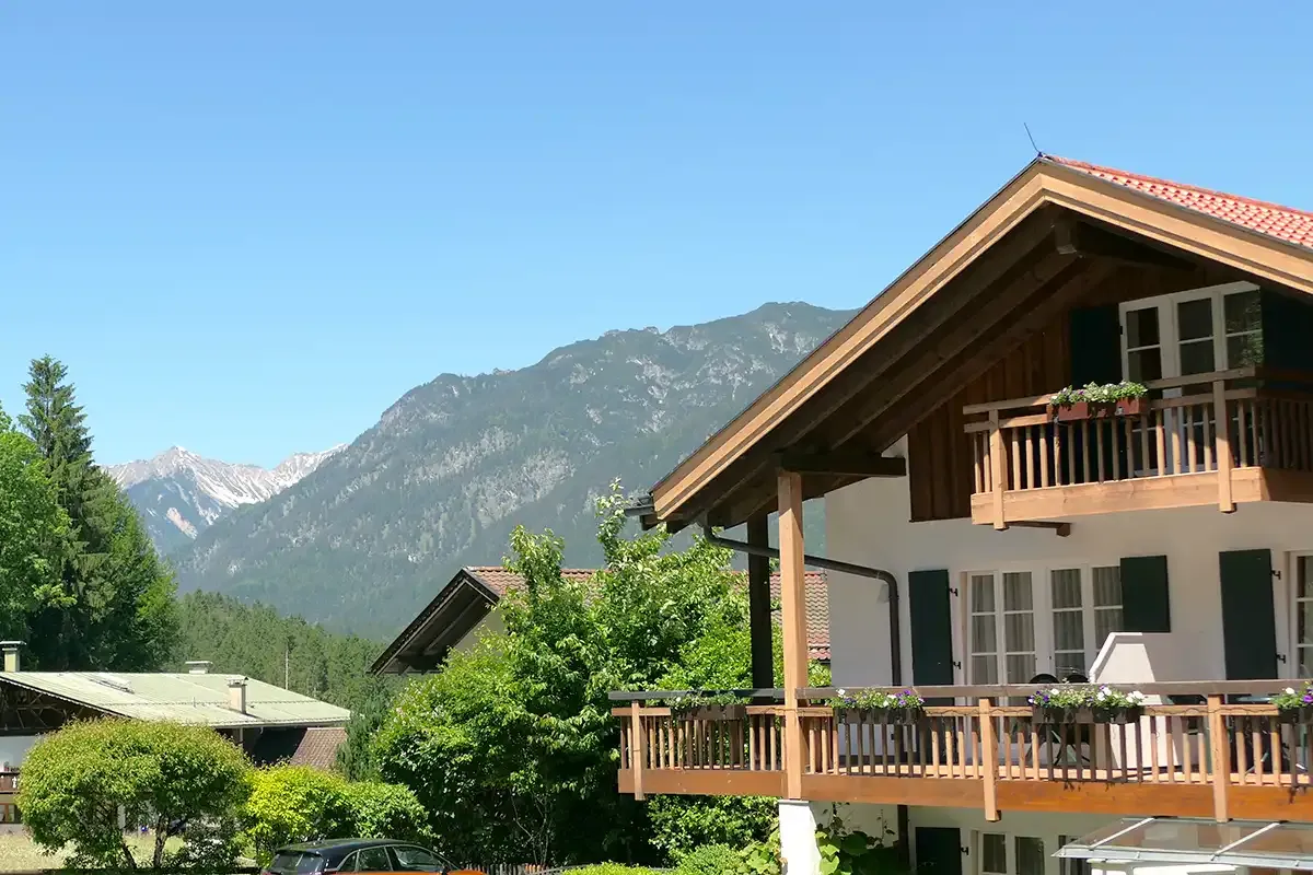 Ausschnitt vom Berghotel Hammersbach mit Holzgeländer, Blumenkörben und den Alpen im Hintergrund.