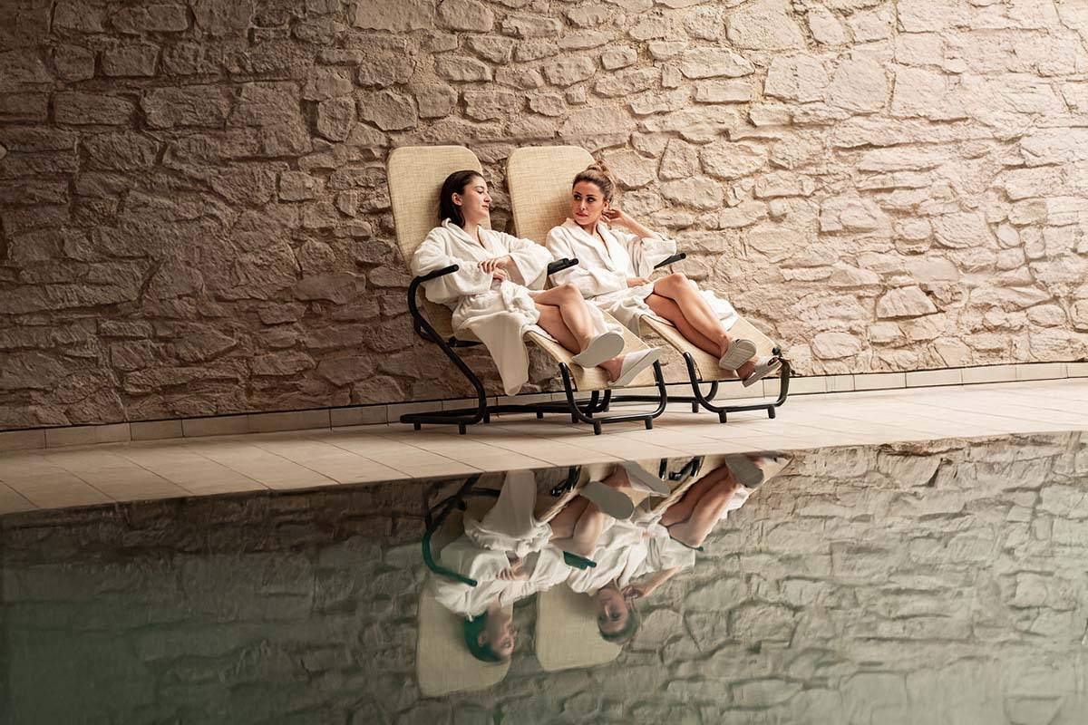 Zwei Frauen sitzen im Bademantel nebeneinander auf einer Liege im Spa-Bereich des Berghotels Hammersbach.