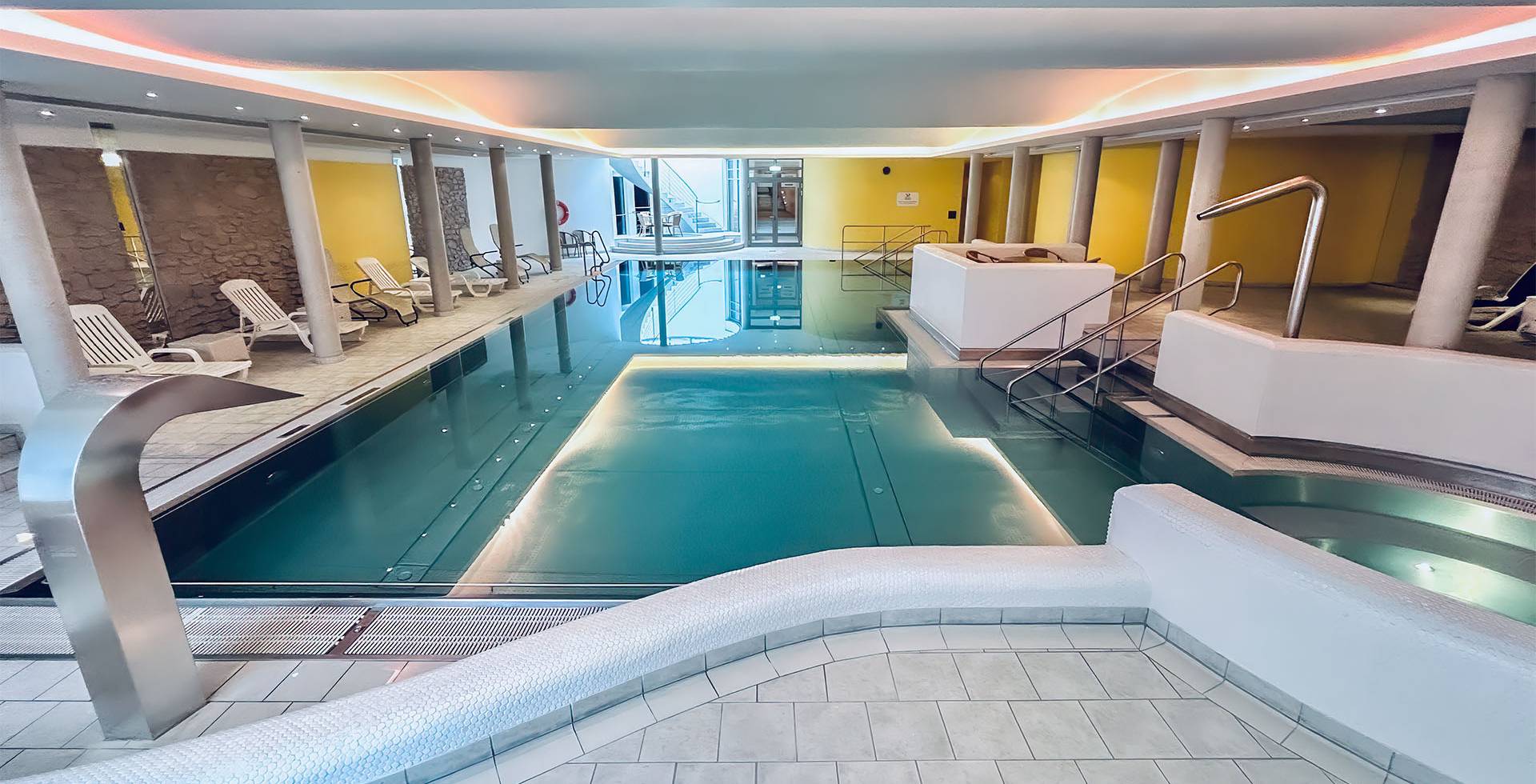 Chlorfreies Schwimmbad mit Gegenstromanlage, umgeben von stilvollen Liegen und sanfter Beleuchtung.