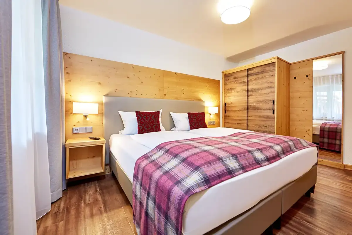 Großes Doppelbett mit gemütlichem Komfort, im Hintergrund ein Kleiderschrank und Spiegel in moderner Holzoptik.