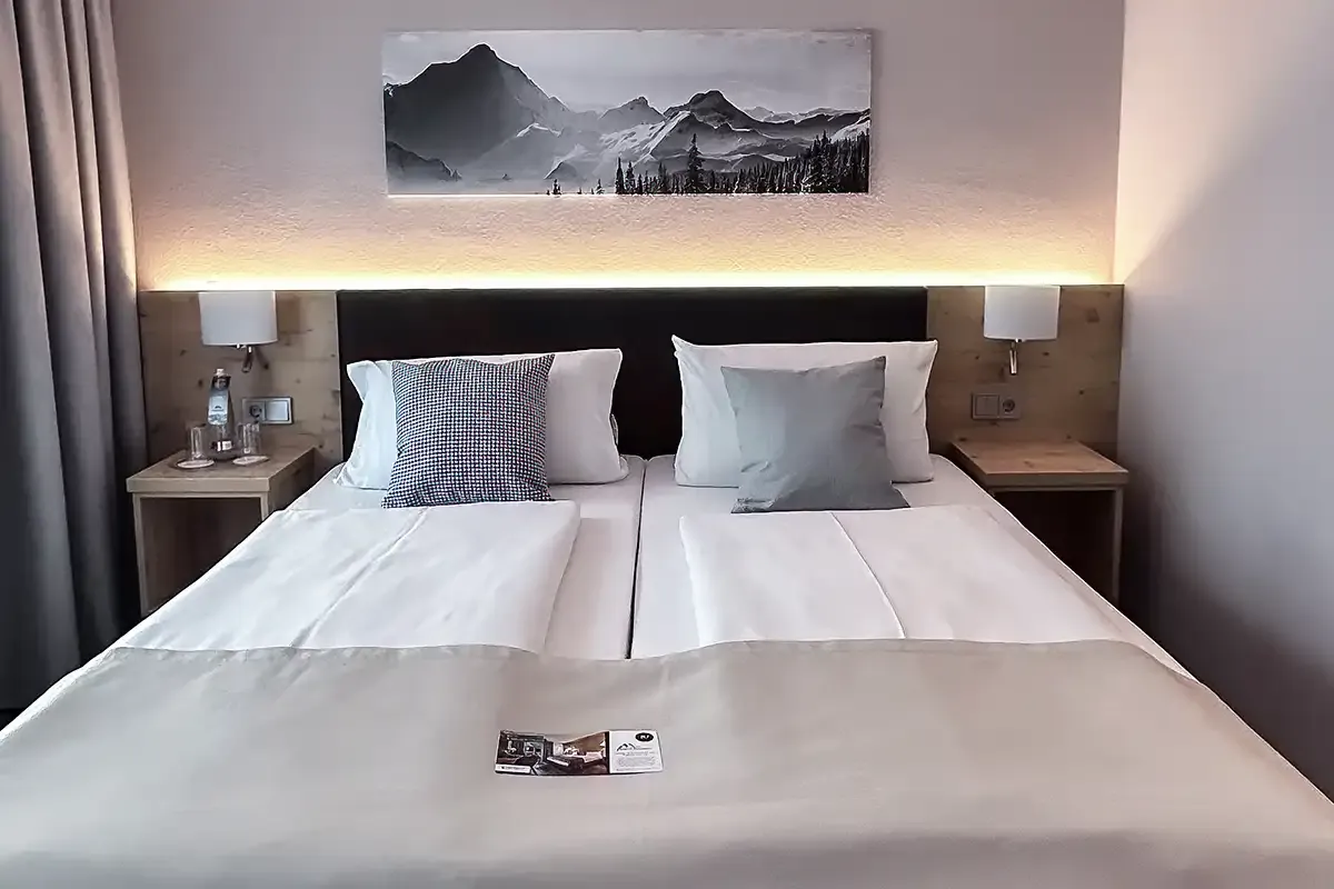 Modernes Doppelbett im Hotelzimmer des Berghotel Hammersbach mit Nachttischen und einem Bild über dem Bett.
