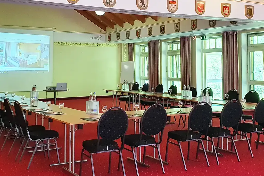 Großer Tagungsraum Zugspitzsaal im Berghotel Hammersbach mit Tischreihen und Leinwand.