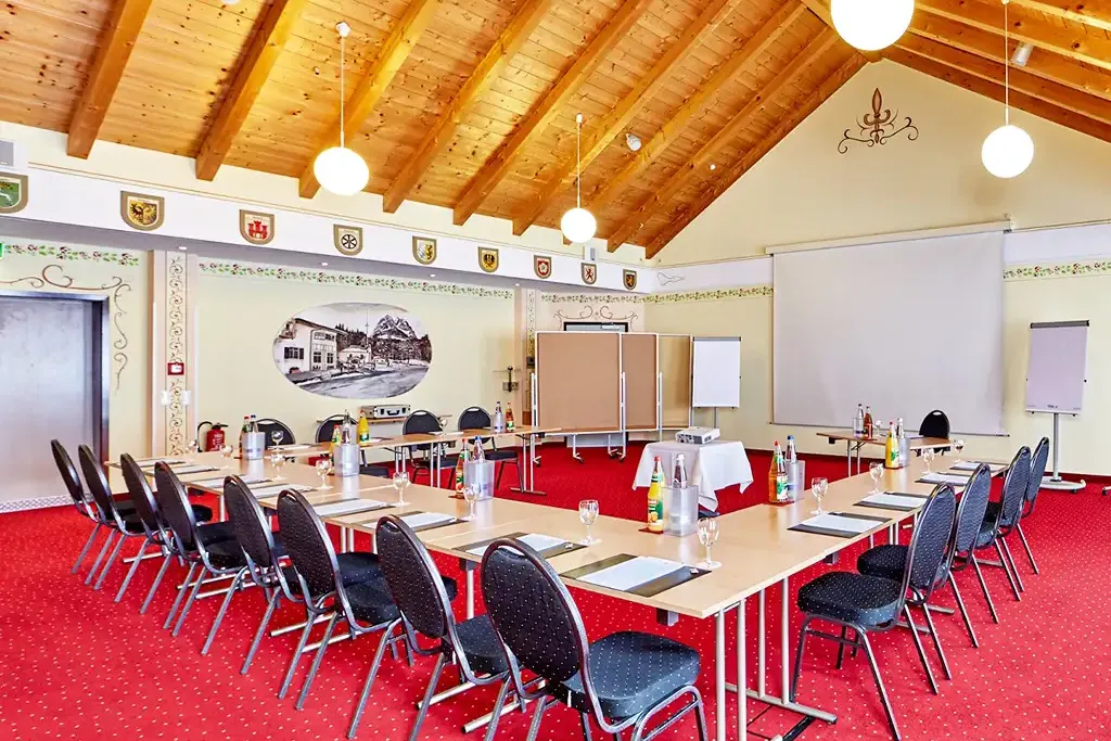 Seminarraum im Berghotel Hammersbach mit Tischreihen, Leinwand und Verpflegung.