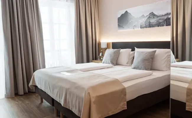 Modernes Hotelzimmer im Berghotel Hammersbach mit Doppelbett an der Wand und modernem Holzboden.
