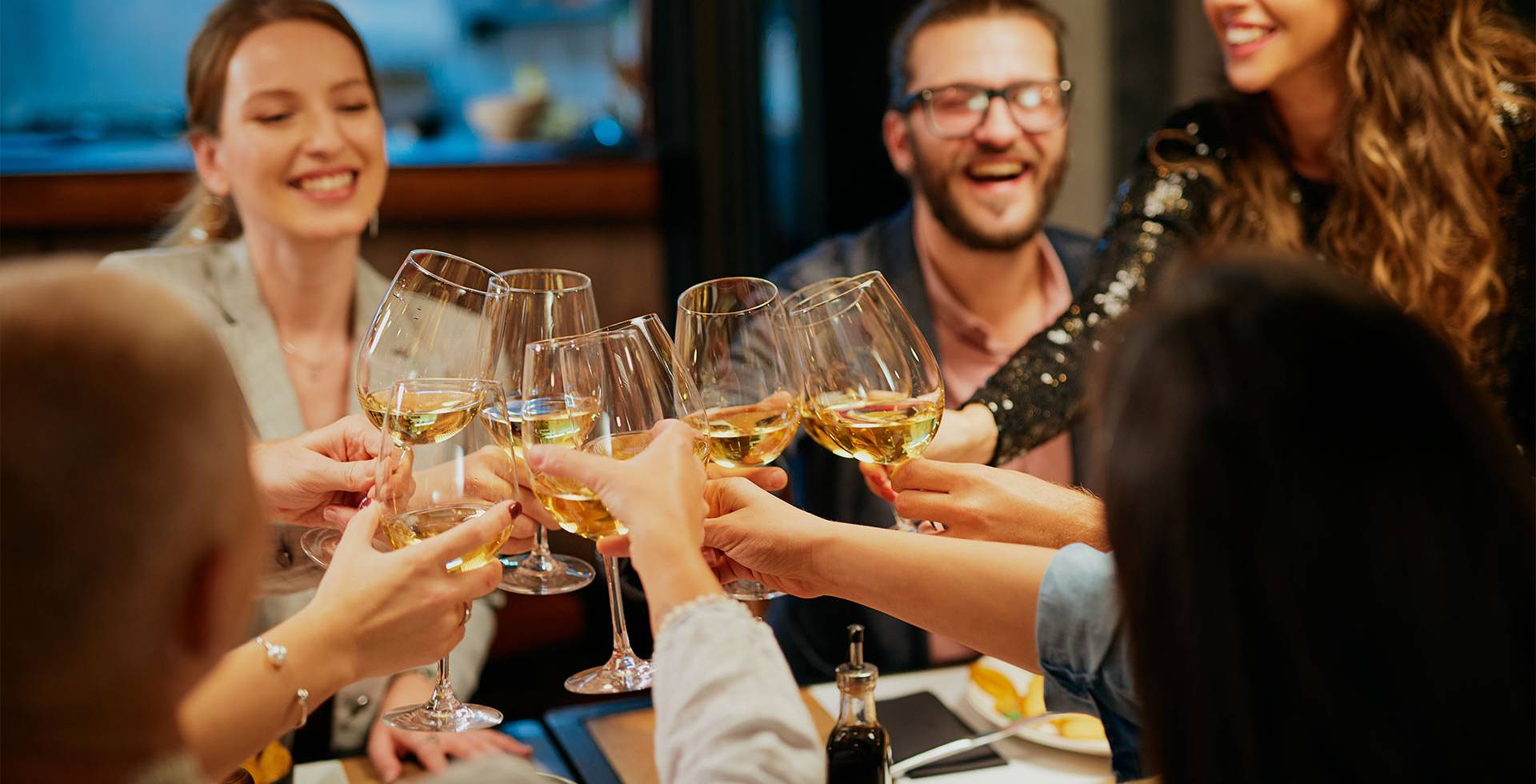 Eine Gruppe sitzt entspannt in schicker Kleidung beieinander und stößt gemeinsam mit Sekt an.