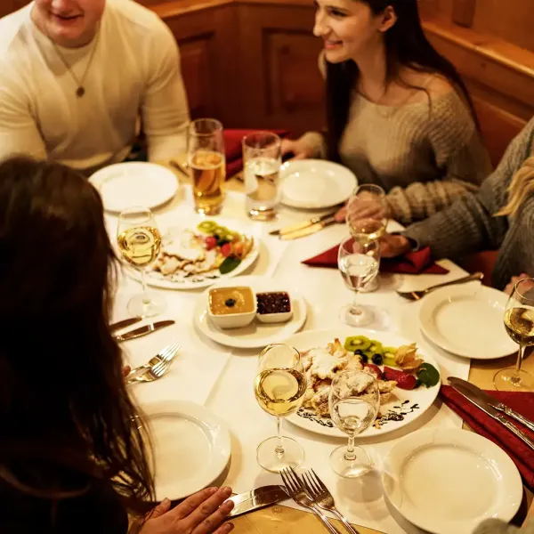 Ein festlich gedeckter Tisch, an dem Gäste sitzen und Kaiserschmarrn mit passenden Obstsorten genießen.