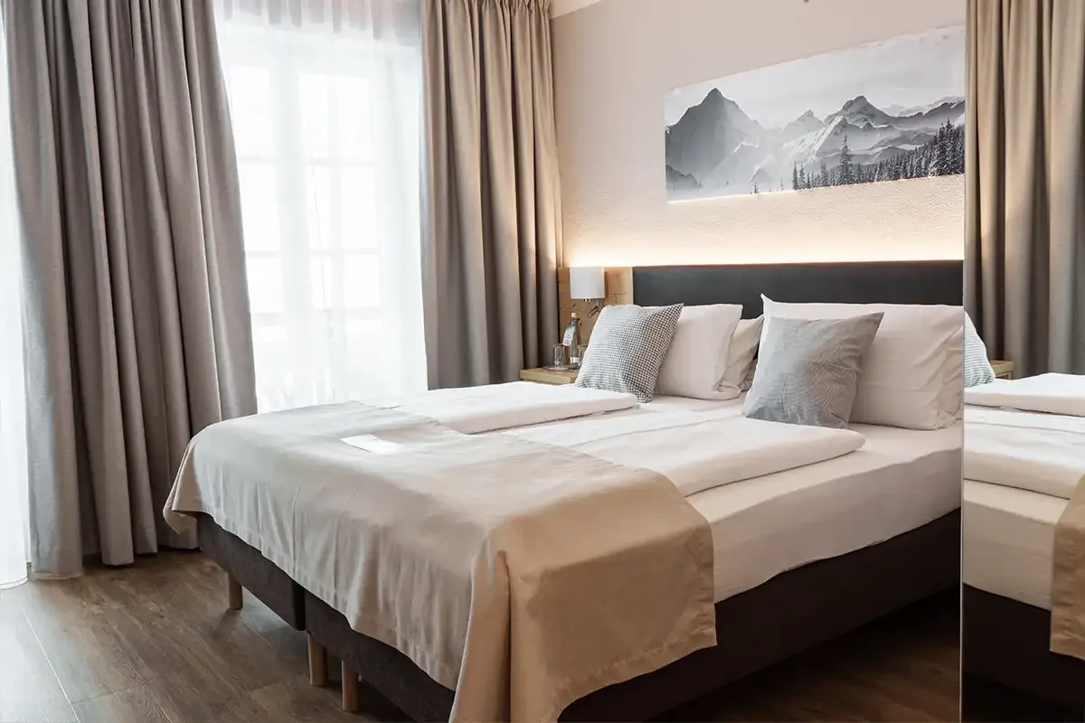 Modernes Hotelzimmer im Berghotel Hammersbach mit Doppelbett an der Wand und modernem Holzboden.