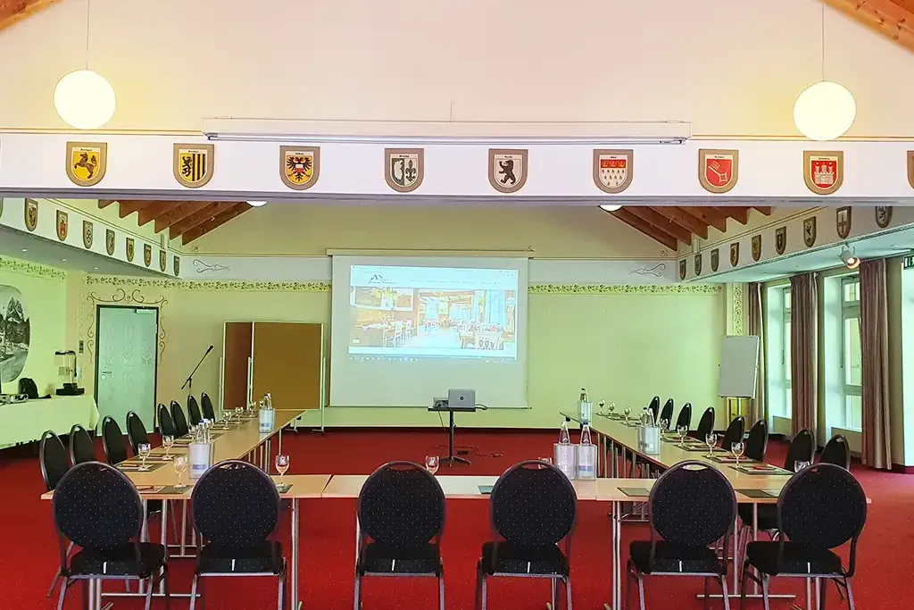 Tagungsraum Zugspitzsaal mit U-förmiger Tischreihe und Leinwand für Übertragungen im Hintergrund.