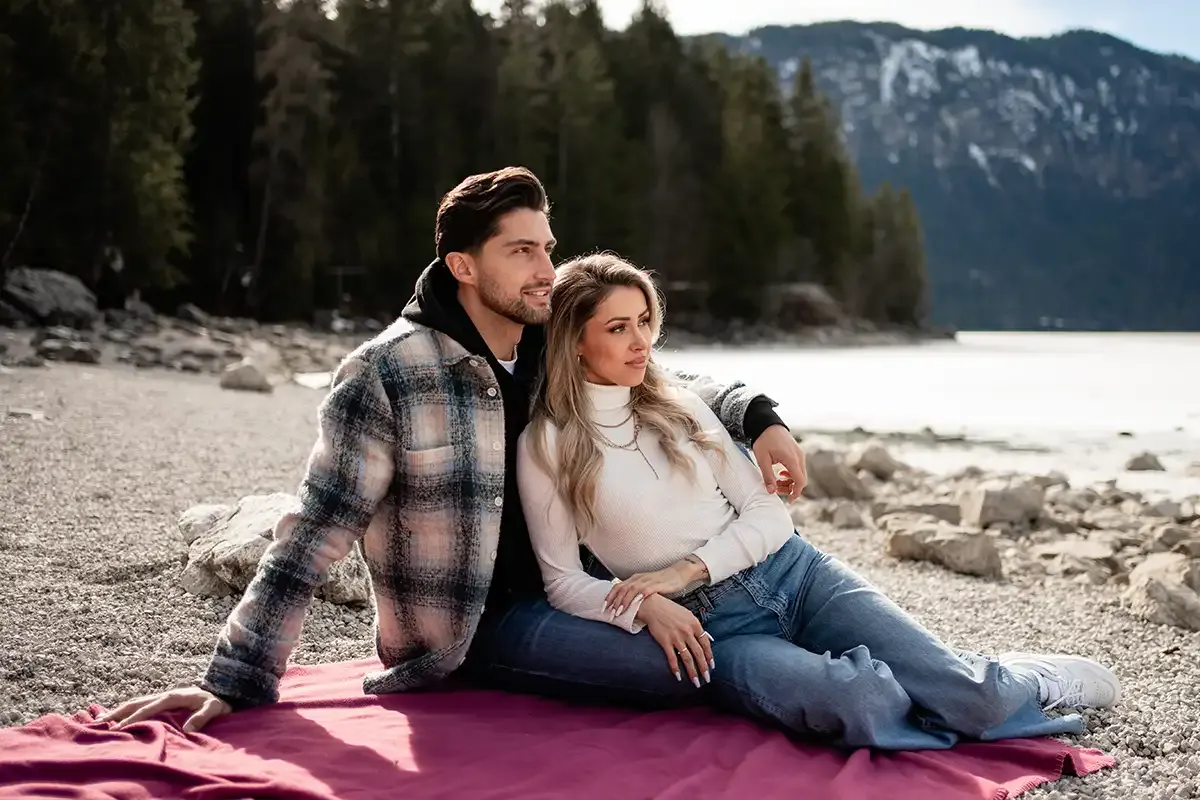 Ein Paar sitzt am Ufer auf einer Decke vor dem Eibsee und genießt die gemeinsame Auszeit mit Bergpanorama.