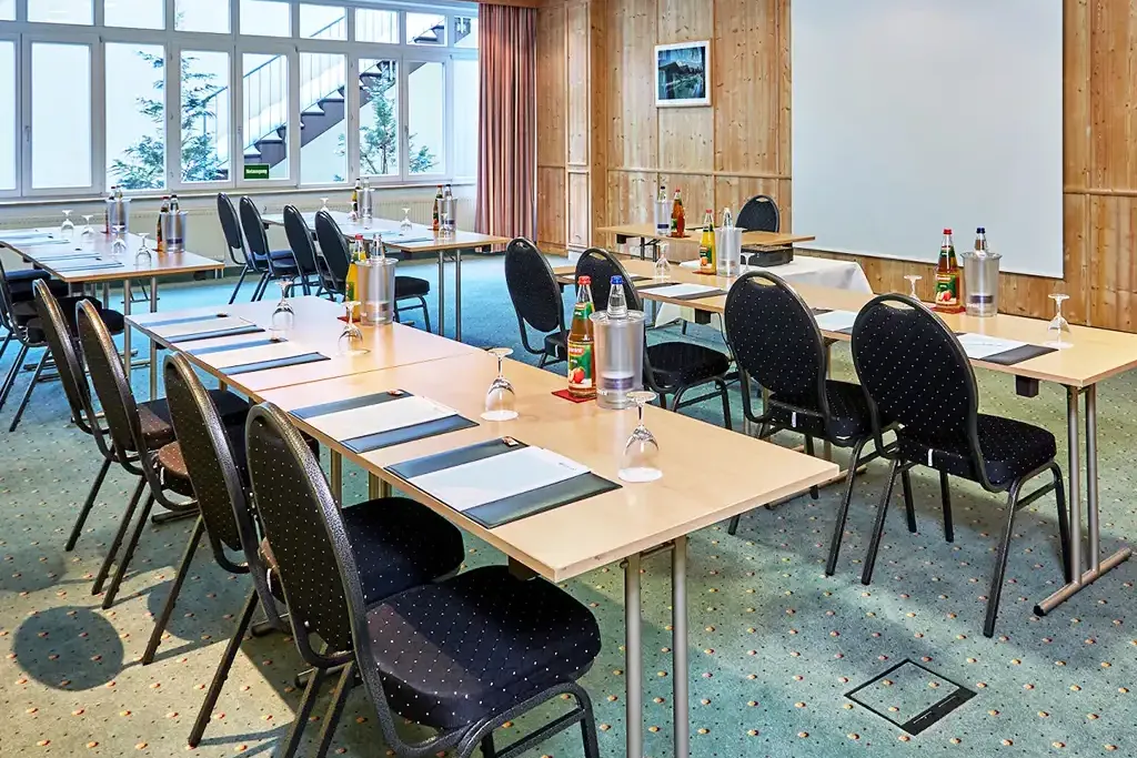 Tagungsraum Waxenstein mit Fensterfront, Tischreihen und Stühlen sowie frischen Getränken auf dem Tisch.