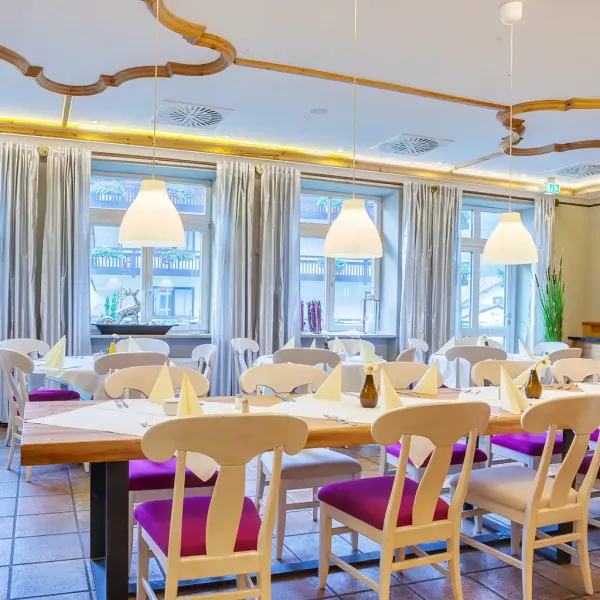 Innenaufnahme des Bistros im Berghotel Hammersbach mit eingedeckten Holztischen und weißen Stühlen.