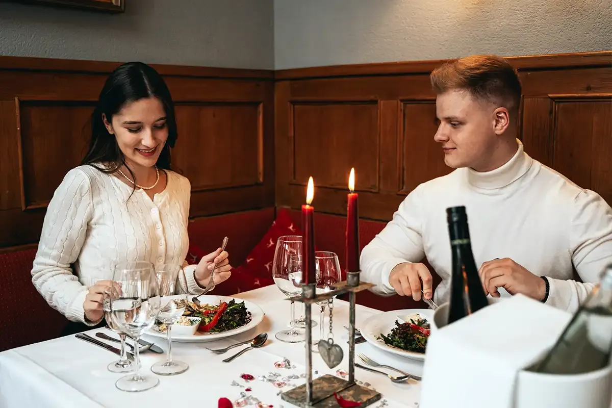Paar sitzt an einem liebevoll eingedeckten Tisch mit Kerzen, Blumen und köstlichen Speisen.