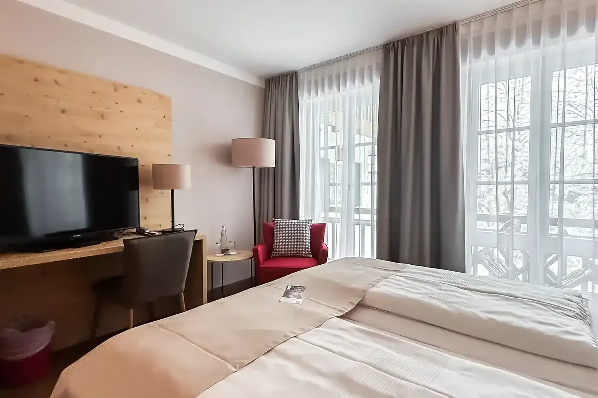 Modernes Hotelzimmer im Berghotel Hammersbach mit TV, Sitzmöglichkeiten und großer Fensterfront.