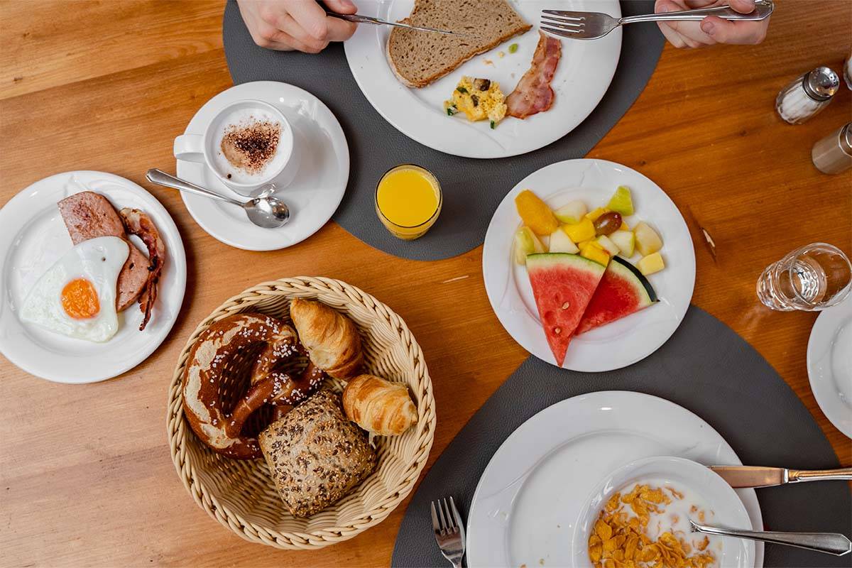 Gedeckter Tisch mit zahlreichen Frühstücksleckereien: Brötchen, Obst, Müsli, Spiegelei und vieles mehr.