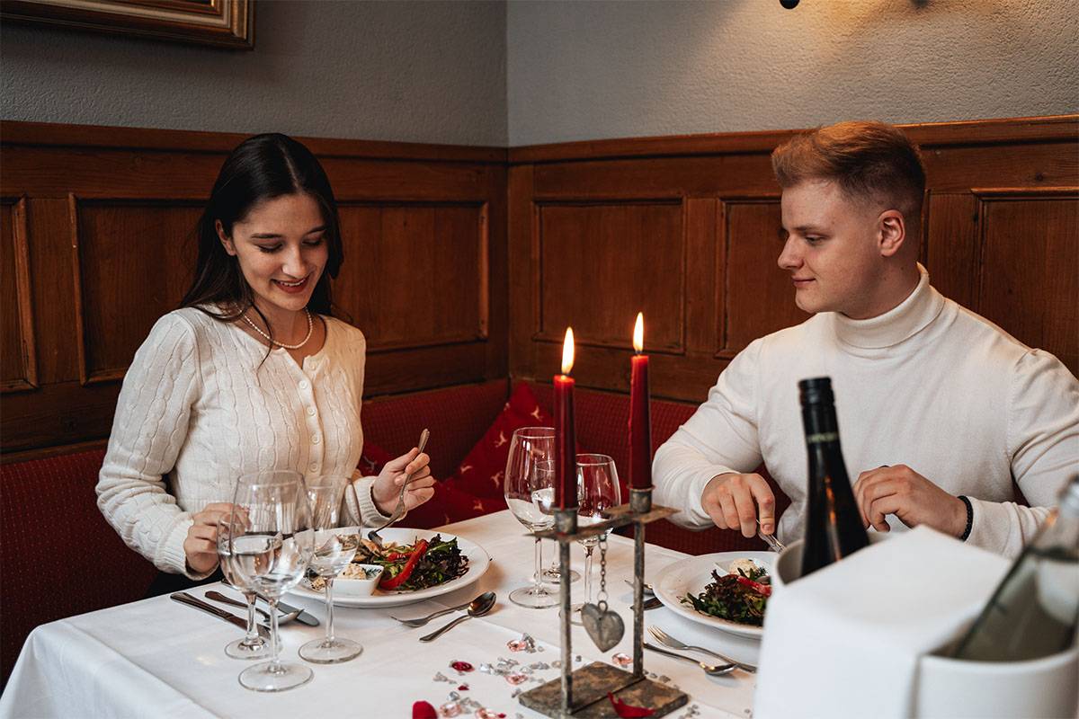 Paar sitzt an einem liebevoll eingedeckten Tisch mit Kerzen, Blumen und köstlichen Speisen.