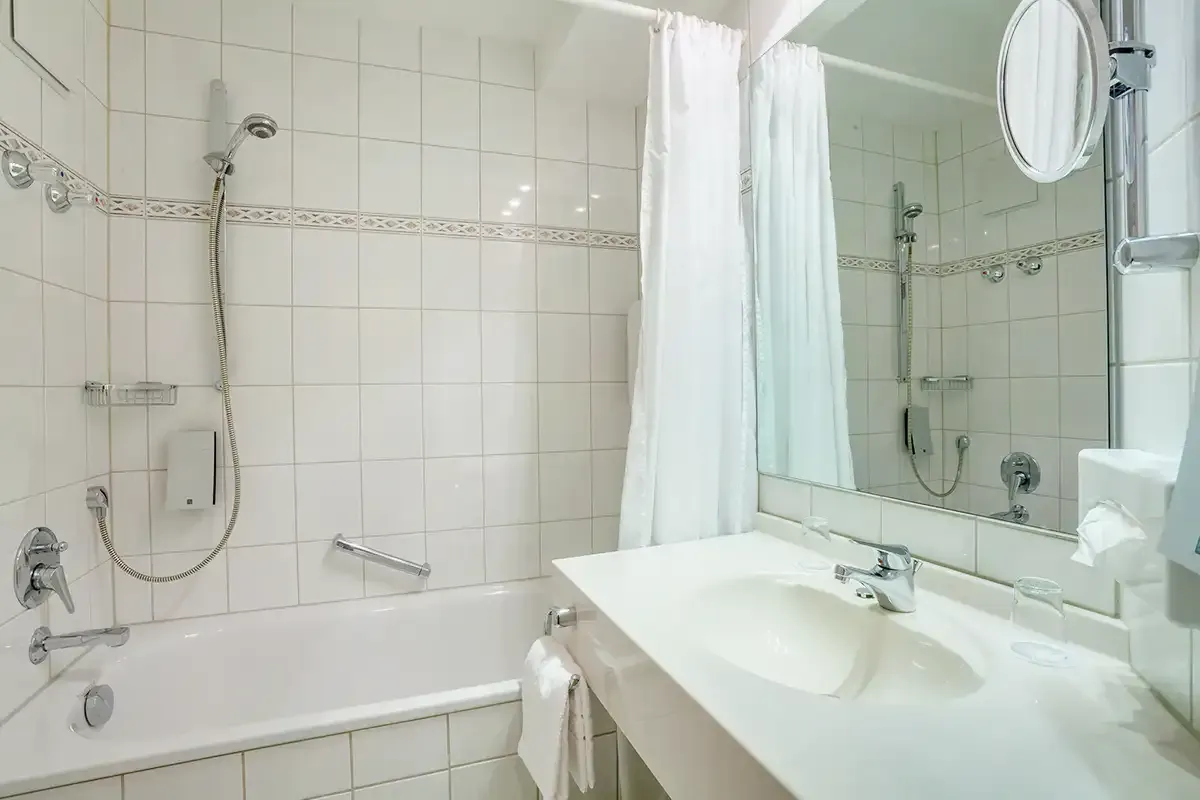 Helles Badezimmer mit einladender Badewanne, großem Waschtisch und Spiegel im Economy-Doppelzimmer des Berghotels Hammersbach.