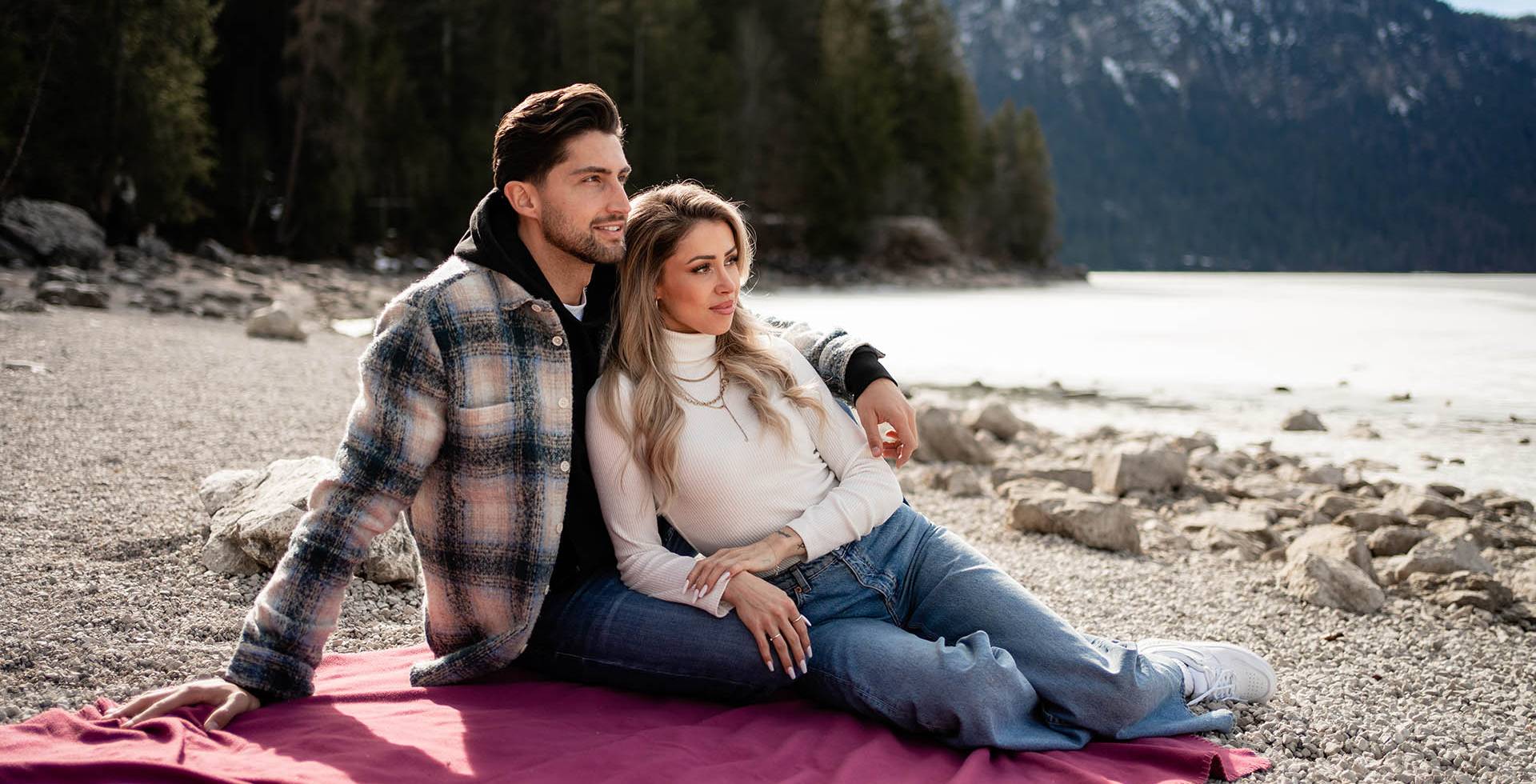Ein verliebtes Paar sitzt auf einer Decke am Ufer des Eibsees und betrachtet die wundervolle Berglandschaft der Alpen.