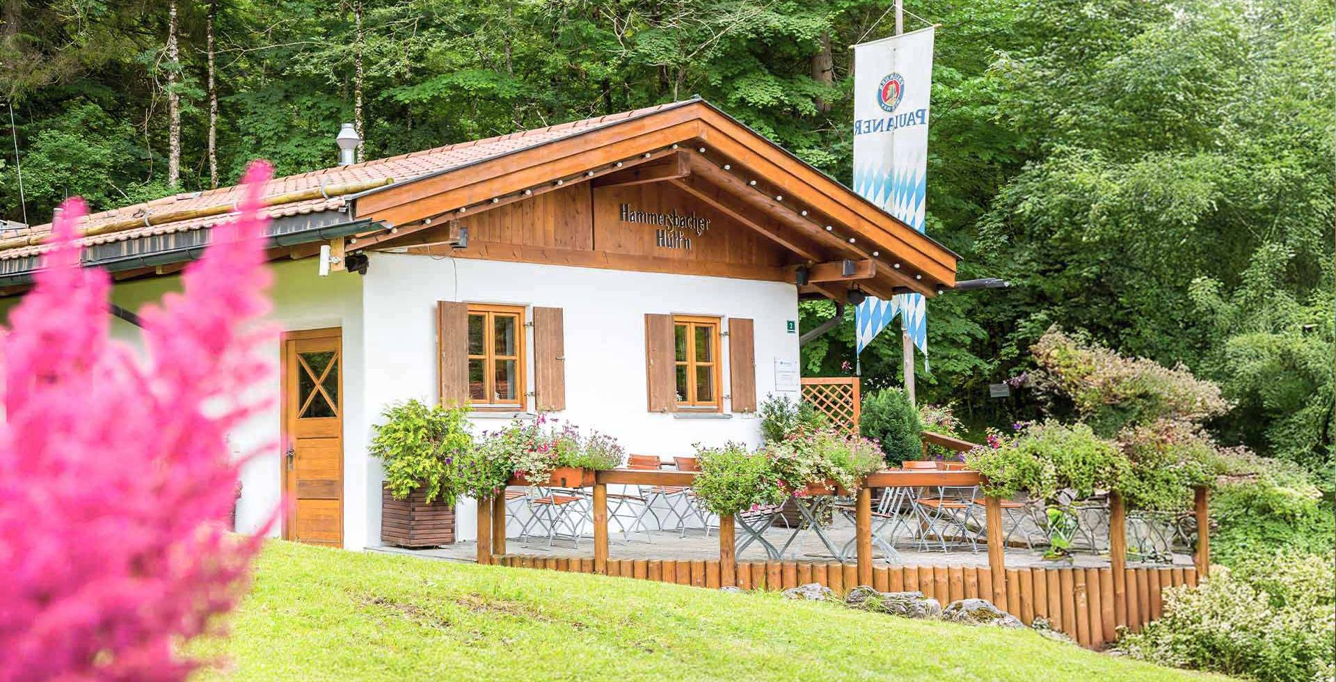 Außenansicht der strahlenden Hammersbach Hütte im Sommer, mit bepflanzten Blumen in Körben am Geländer.