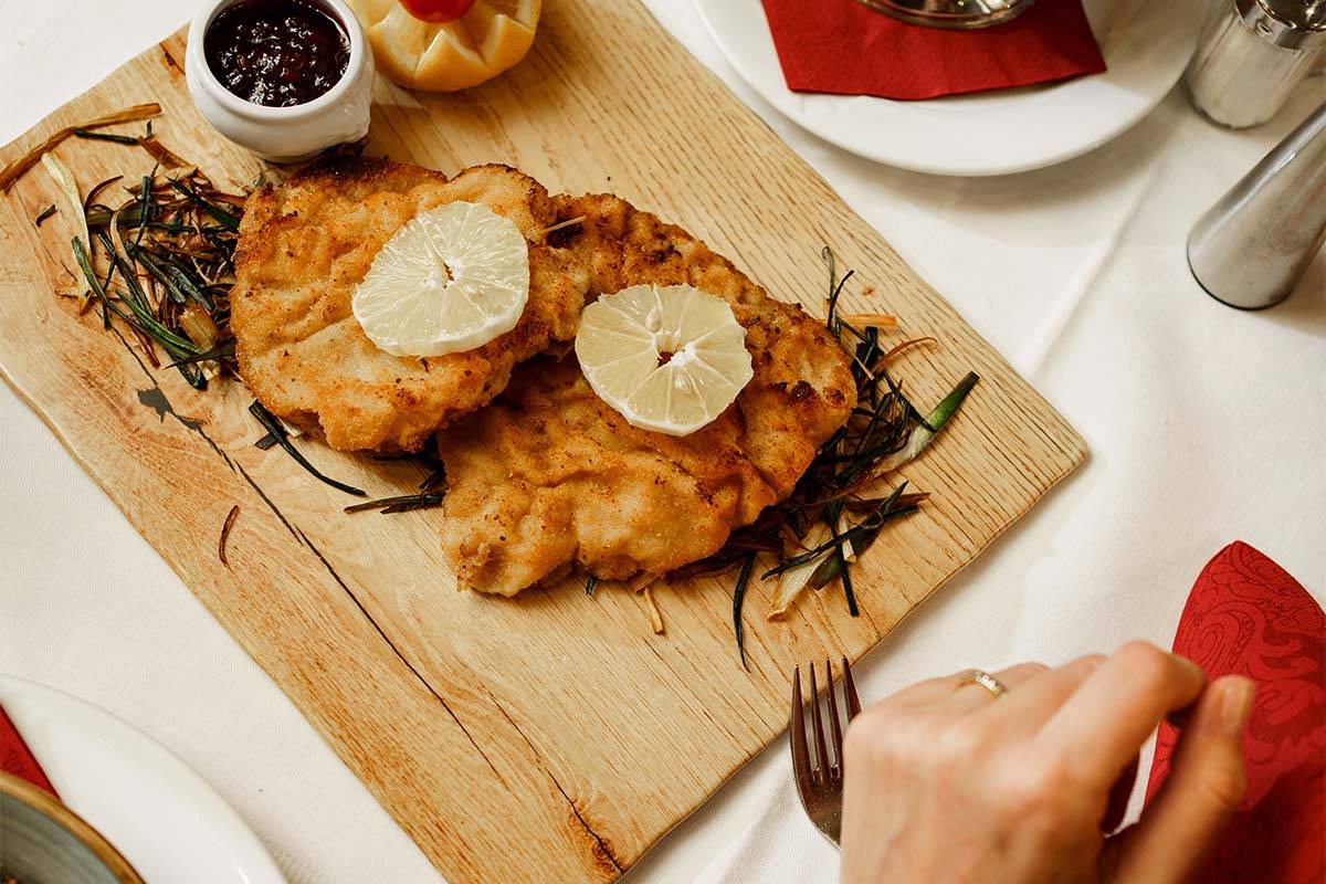Auf einem gedeckten Tisch in der Hammersbach Hütte sind auf einem Holzbrett zwei Schnitzel serviert.