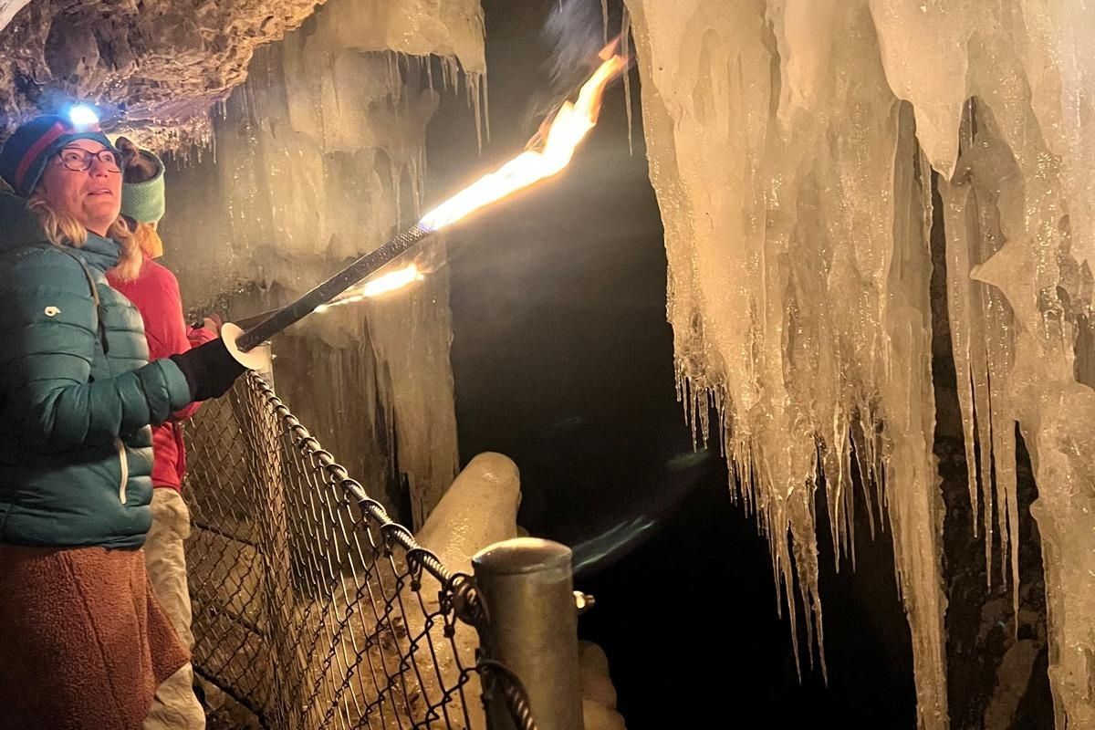 Eine Gruppe von Menschen läuft hintereinander an einem Felsen vorbei und hält Fackeln in der Hand.